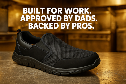 Black slip-on work shoe displayed on a worn concrete surface in a warm industrial kitchen setting. Bold white text above the shoe reads: “BUILT FOR WORK. APPROVED BY DADS. BACKED BY PROS.”